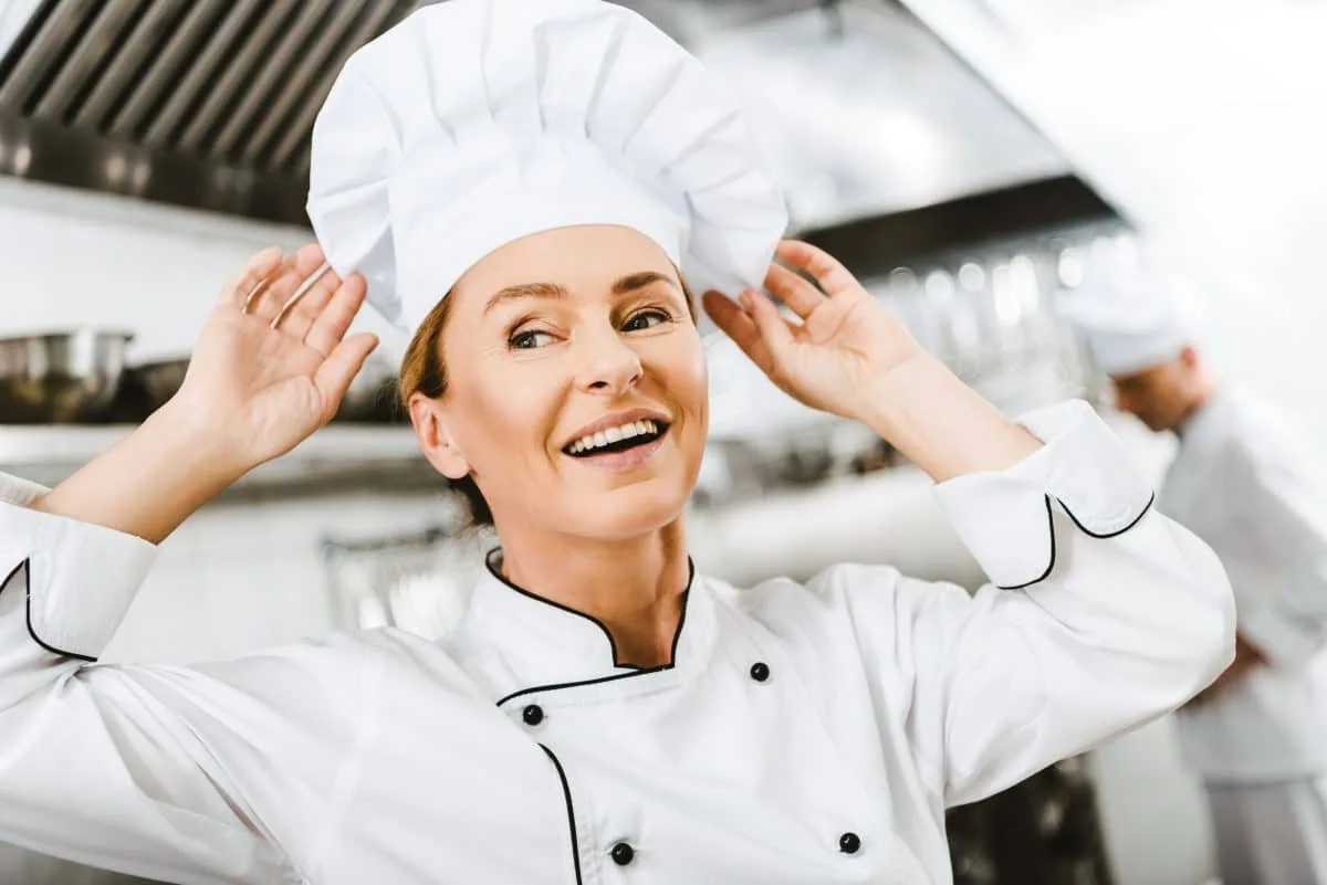 Chef souriante ajustant son tablier en cuisine professionnelle