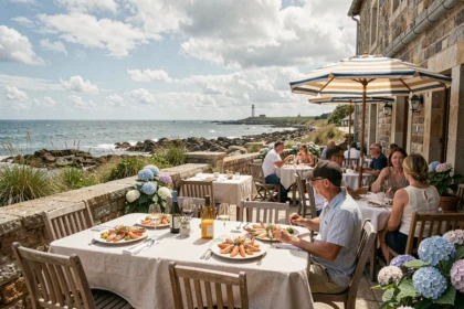 Terrasse de restaurant bretonne avec vue sur la mer, tables en bois, parasols rayés et clientèle dégustant des fruits de mer face à l'Atlantique